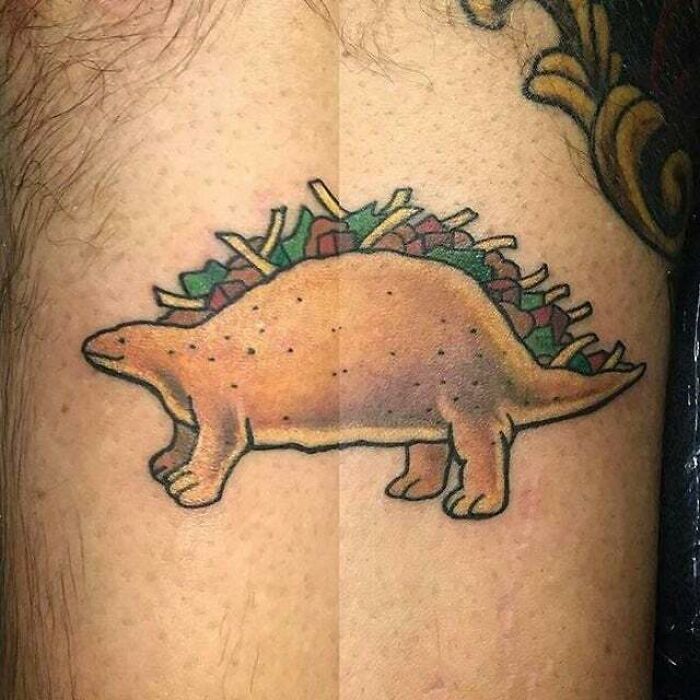 Tattoo of a stegosaurus resembling a taco, combining elements of trippy and psychedelic art on the skin.