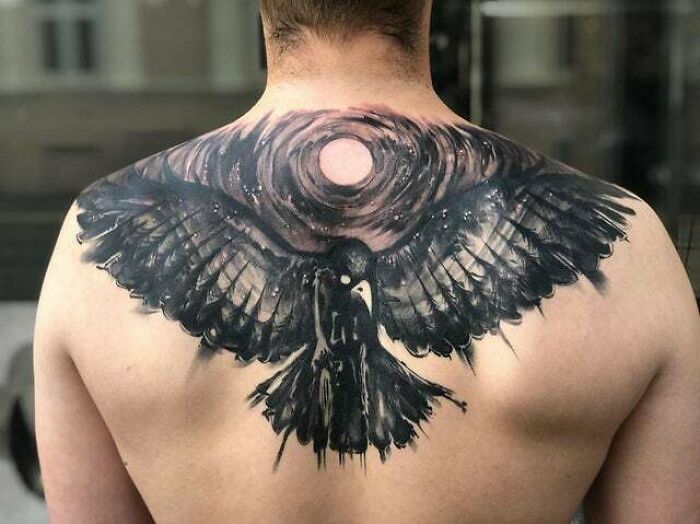 Back tattoo of a trippy black raven, wings spread, with a cosmic swirl in the background.
