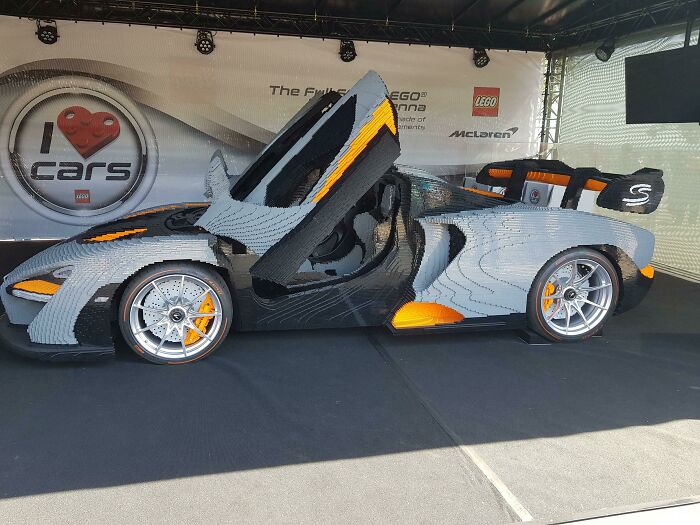 LEGO builds showcasing a detailed life-size sports car replica with open gullwing door in a display setting