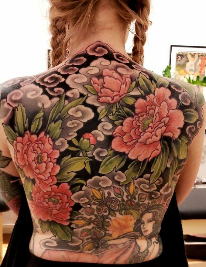 Psychedelic art-inspired tattoo featuring vibrant peonies and swirling patterns on a woman's back.