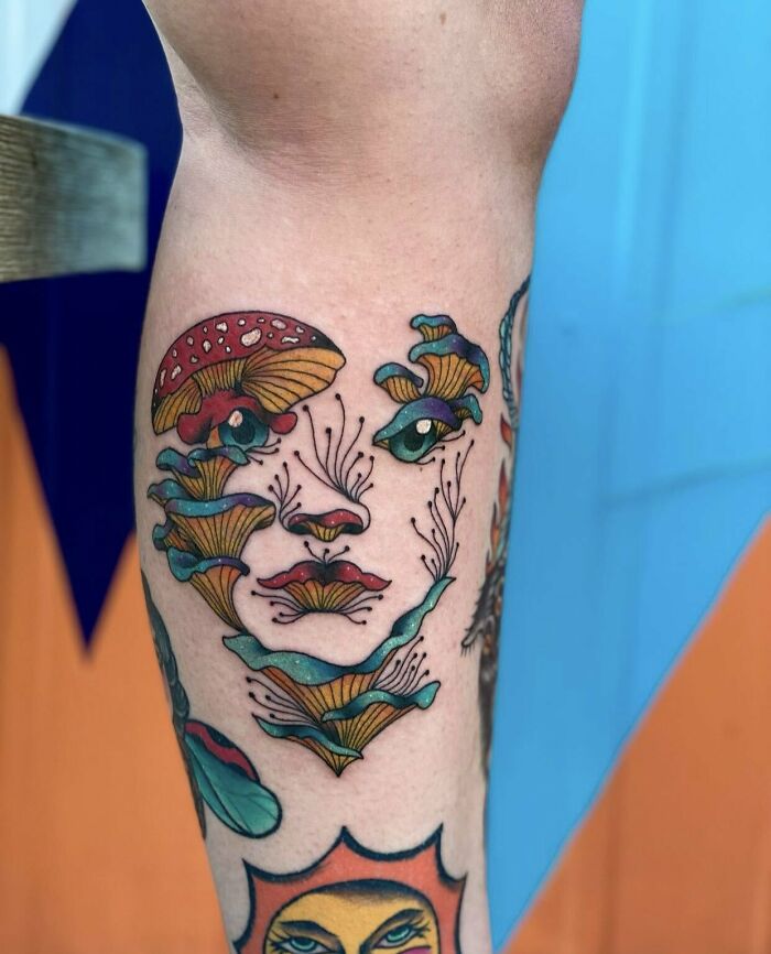 Psychedelic art tattoo with colorful mushrooms forming a face on a person's leg.