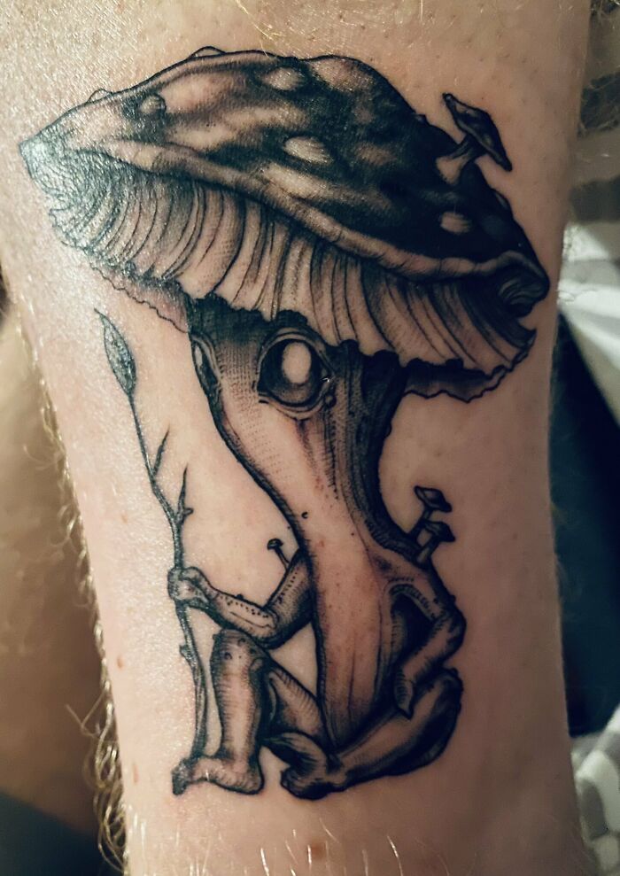 Trippy tattoo of a whimsical mushroom character holding a branch.