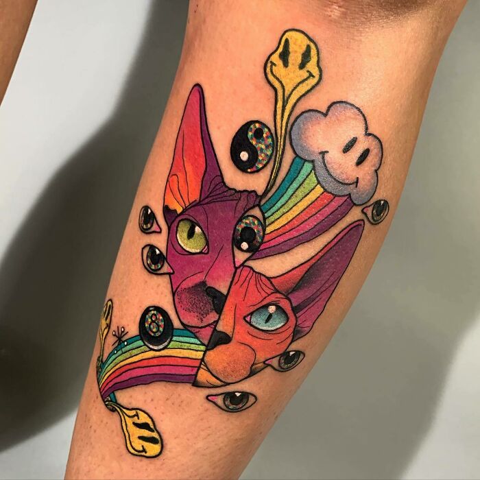 Colorful trippy tattoo with cats, rainbows, and psychedelic elements on arm.
