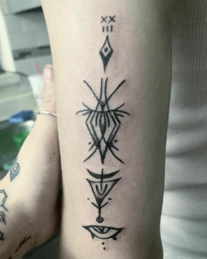 Trippy symbols arm tattoo with intricate geometric and eye motifs.