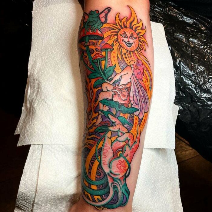 Colorful trippy tattoo of a fairy with mushrooms, sun, and frogs on an arm sleeve.