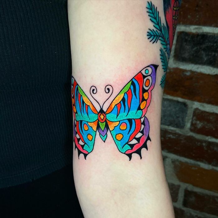 Colorful psychedelic butterfly tattoo on an arm.