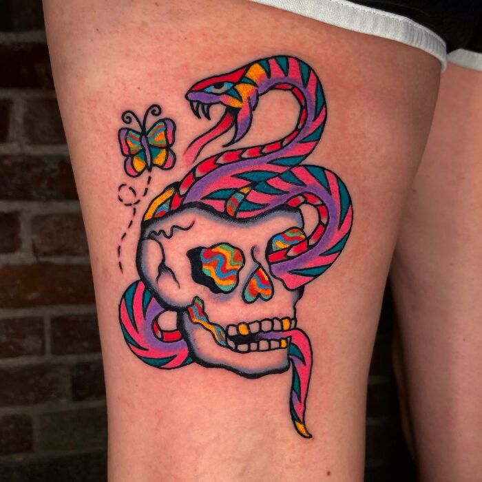 Psychedelic art tattoo featuring a colorful snake, skull, and butterfly design on the skin.