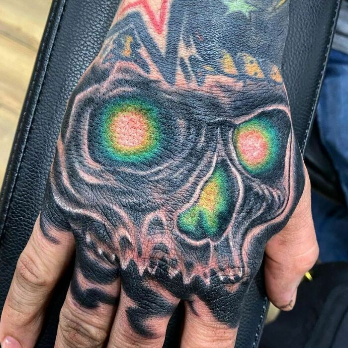 Trippy tattoo of a spooky skull with glowing eyes on a hand.