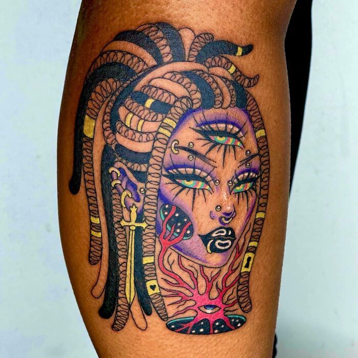 Psychedelic art tattoo featuring a colorful, abstract face with multiple eyes and braided hair.