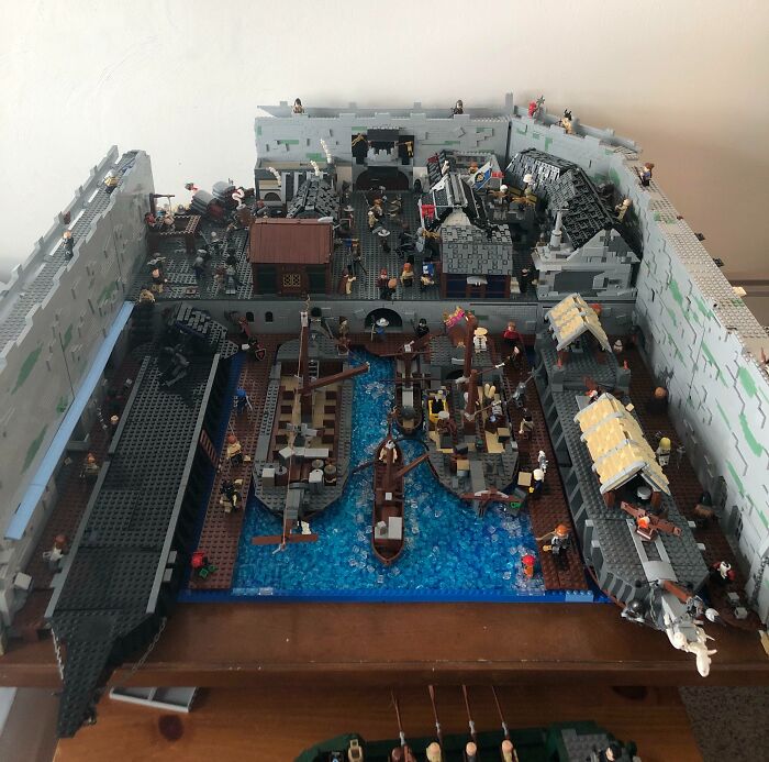 Intricate LEGO builds depicting a detailed medieval harbor scene with ships, buildings, and minifigures in a walled fortress.