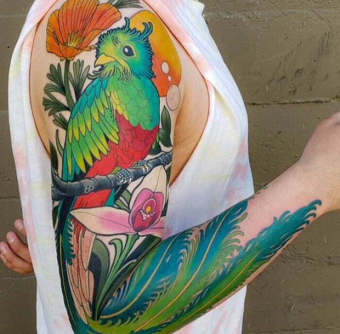 Psychedelic art tattoo of a vibrant bird on a person's arm, featuring colorful feathers and floral elements.