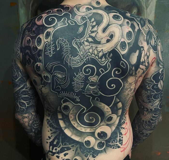 Full back tattoo with trippy eyes and octopus design, blending intricate patterns in a surreal style.