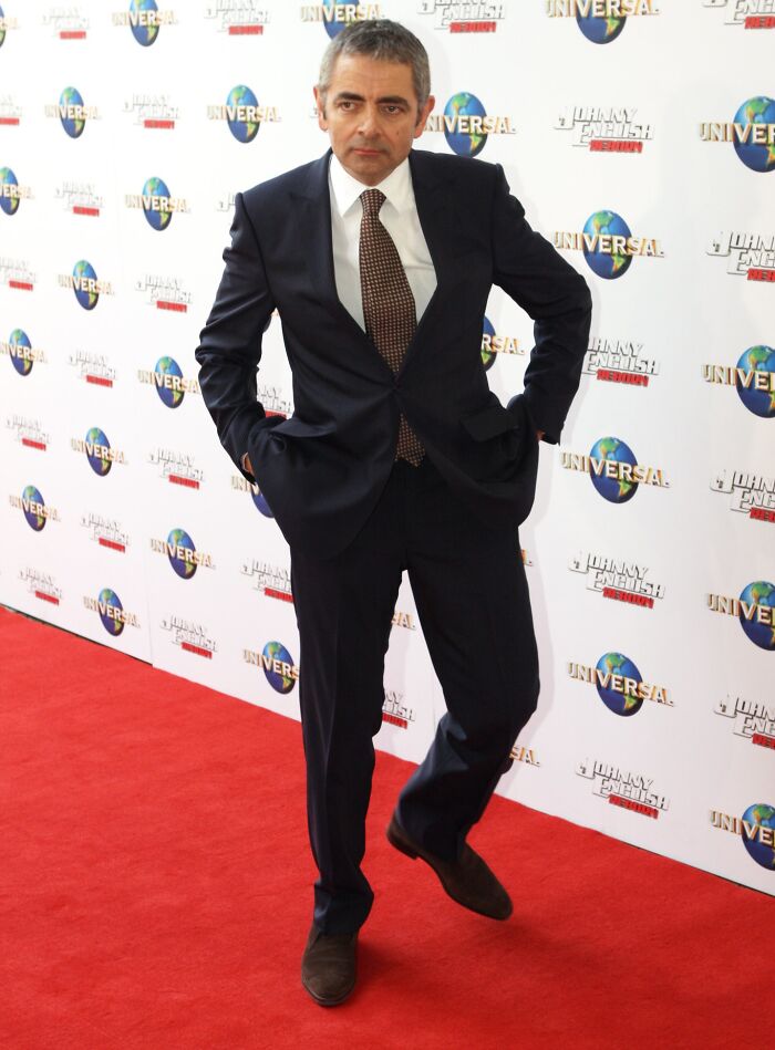 Rowan Atkinson in a dark suit posing confidently on the red carpet, one of the smartest celebrities known for intelligence.