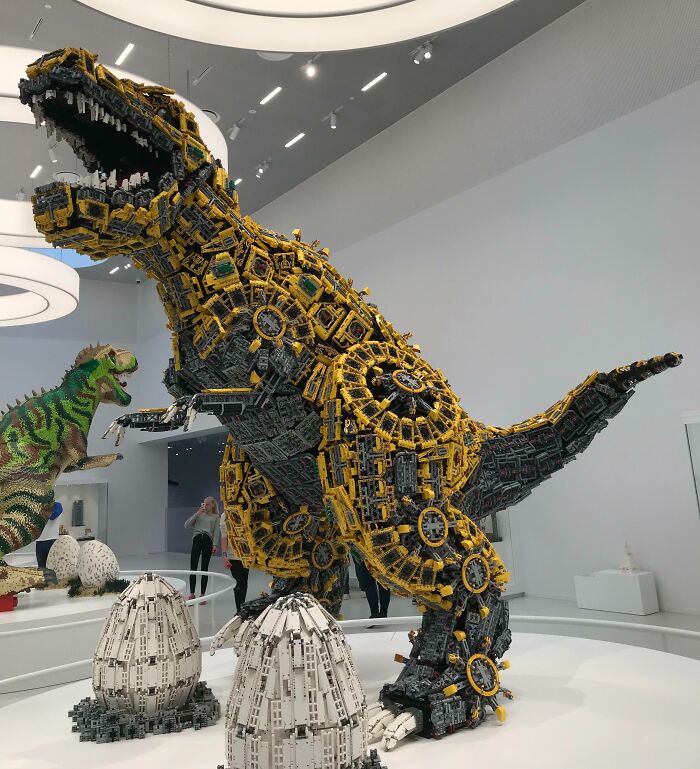 Large intricate LEGO dinosaur sculpture with mechanical details and eggs displayed in a modern gallery showcasing incredible LEGO builds.