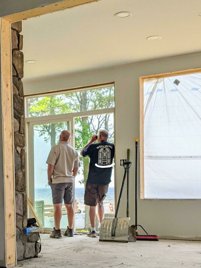 Two men stand indoors, one with a shirt labeled "WELL HUNG," looking out a glass door; a cringe-worthy moment captured.