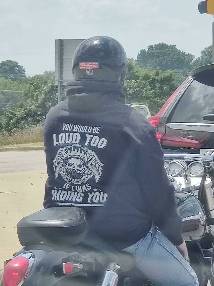 Rider wearing a helmet and hoodie with humorous text, capturing a cringe-worthy moment on a motorcycle.