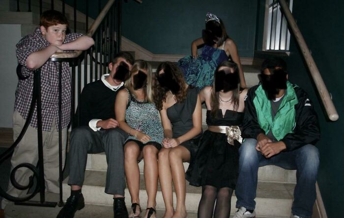 Group of teenagers awkwardly posing on stairs, with one boy standing apart, creating a cringe-worthy photo moment.