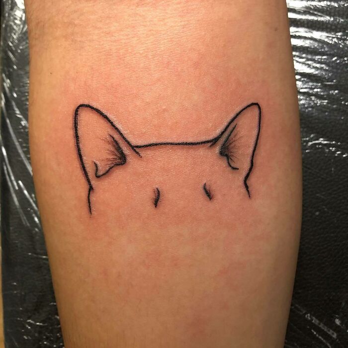 Minimalist pet tattoo featuring a cat's ears and head outline on skin, celebrating human-pet bond.
