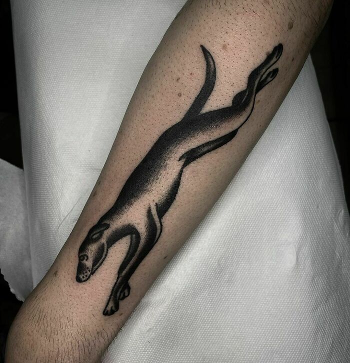 Pet tattoo of a leaping black dog on an arm, symbolizing the bond between humans and their pets.