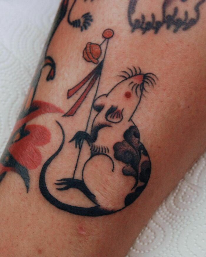 Tattoo of an adorable mouse holding a flag, showcasing a creative pet design on skin.