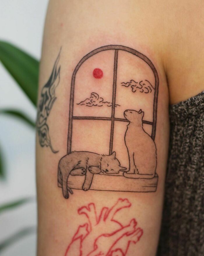 Pet tattoos featuring two cats sitting by a window with a red sun and clouds, inked on an arm.