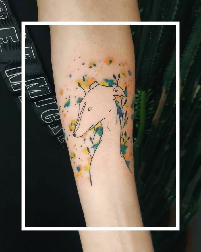 Pet tattoo of a dog with colorful floral accents on the arm.