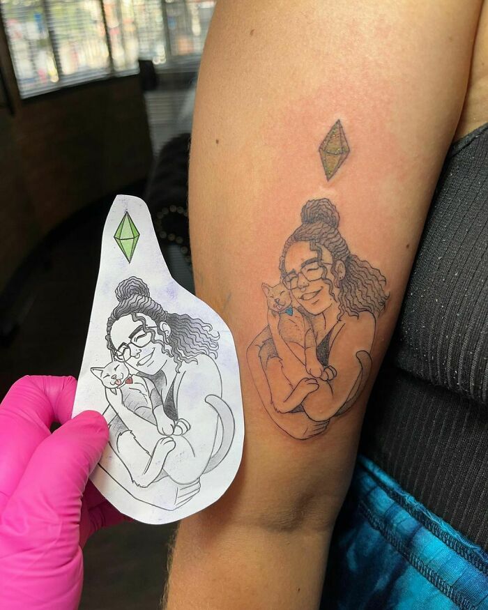 Pet tattoo on arm showing a person with glasses cuddling a cat, with matching tattoo sketch in hand.