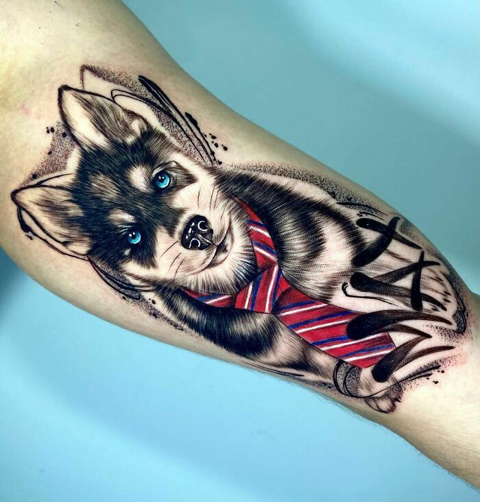 Pet tattoo of a husky wearing a red striped tie on a person's forearm, highlighting beautiful furry friend art.
