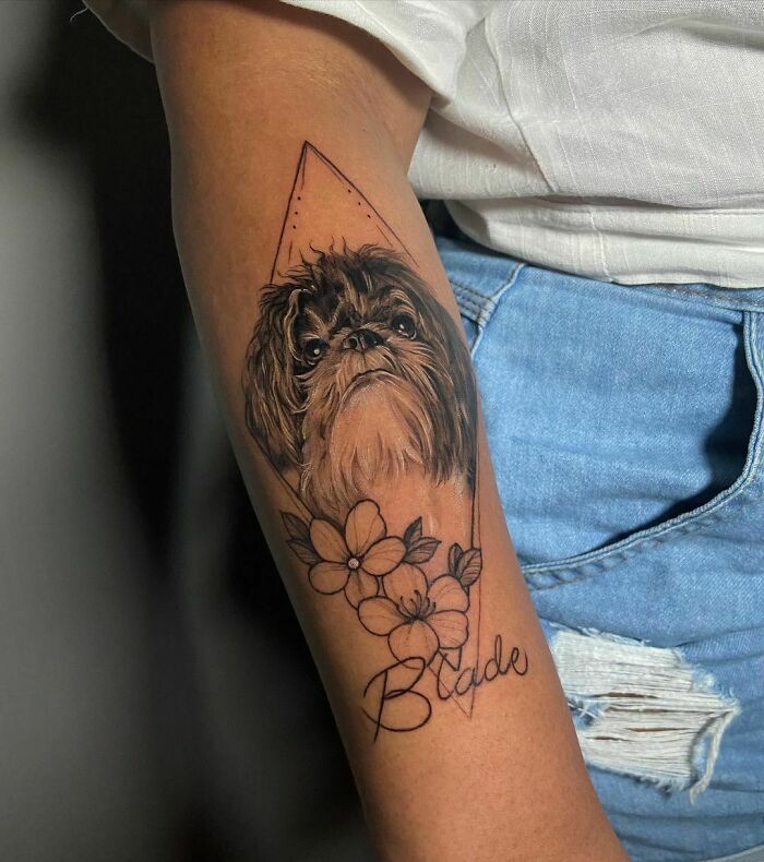 Pet tattoo of a dog with flowers and the name "Blade" on a person's arm.