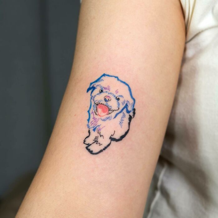 Pet tattoo of a fluffy dog with a blue outline on an arm, celebrating furry friends.