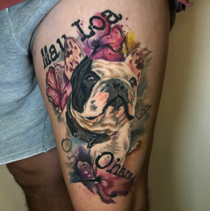 Adorable pet tattoo of a French bulldog with vibrant flowers and lettering on a person's thigh.