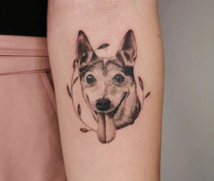 Realistic pet tattoo of a happy dog with its tongue out, framed by leaves, celebrating furry friends.