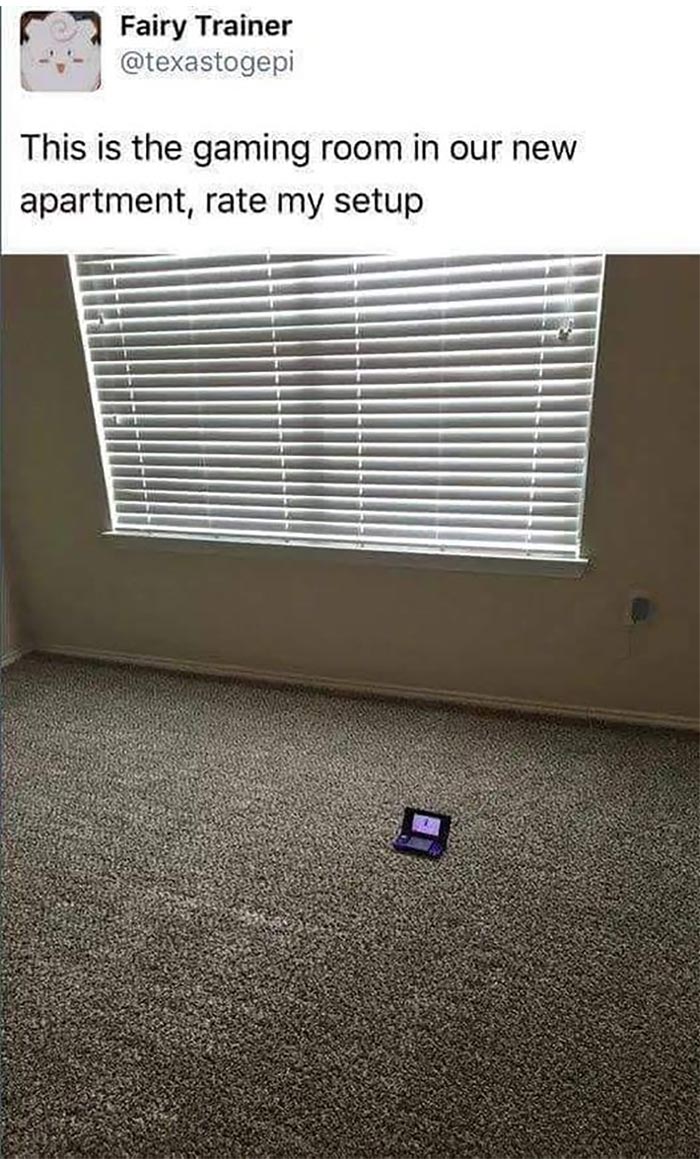 Minimalist gaming setup with a single handheld console on carpeted floor under a large window with closed blinds.