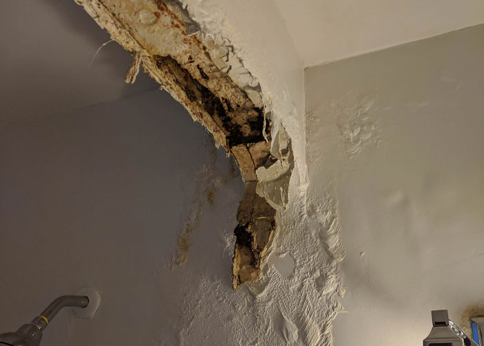 Exposed damaged drywall and wood inside a wall showing homeowning repair needs in an indoor space.