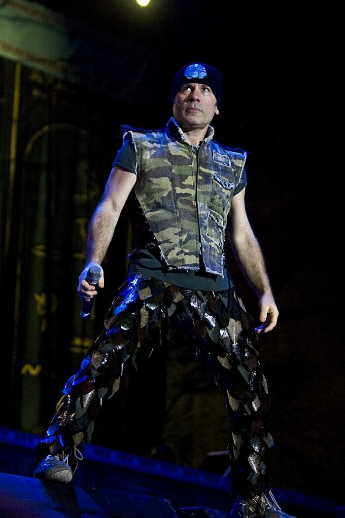 Male celebrity wearing a camouflage vest and unique patterned pants performing on stage, showcasing the smartest celebrities.
