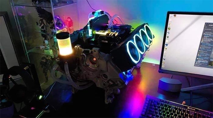 Gaming setup featuring a custom PC built inside an engine block with colorful RGB lighting and multiple cooling fans.