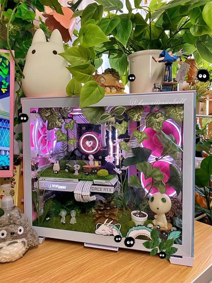 Gaming setup with plants, pink LED fans, and whimsical decorations featuring RTX graphics card and animated character figurines.