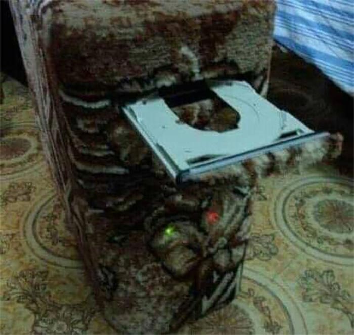 Cursed gaming setup featuring a PC tower camouflaged with a patterned fabric matching the surrounding couch and carpet.