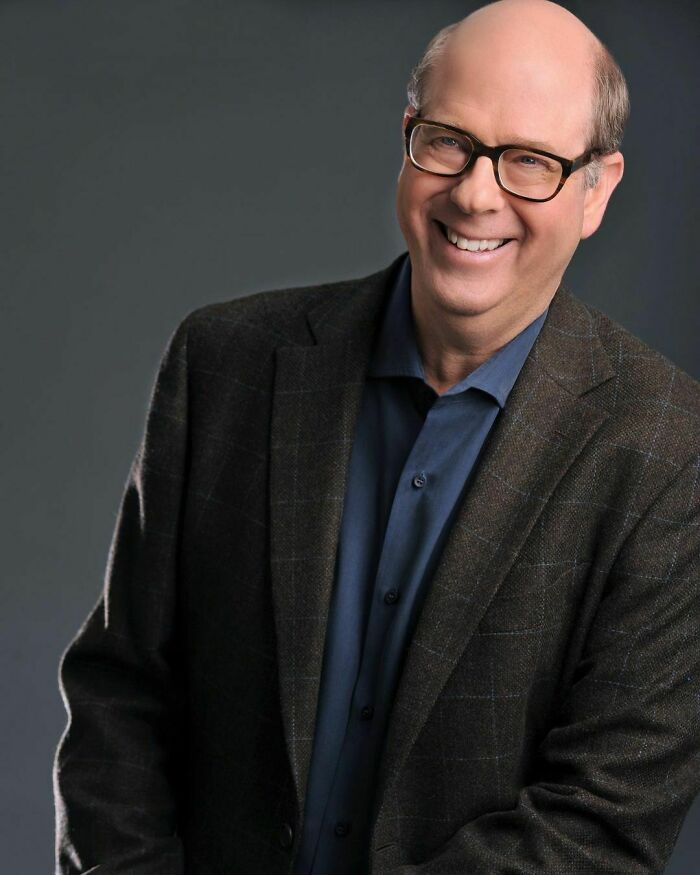 Smiling man wearing glasses and a blazer, representing one of the smartest celebrities known for talent and intelligence.