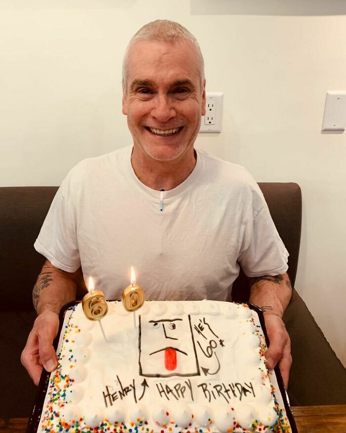 Smiling intelligent celebrity celebrating 60th birthday holding a cake with candles and handwritten decoration.