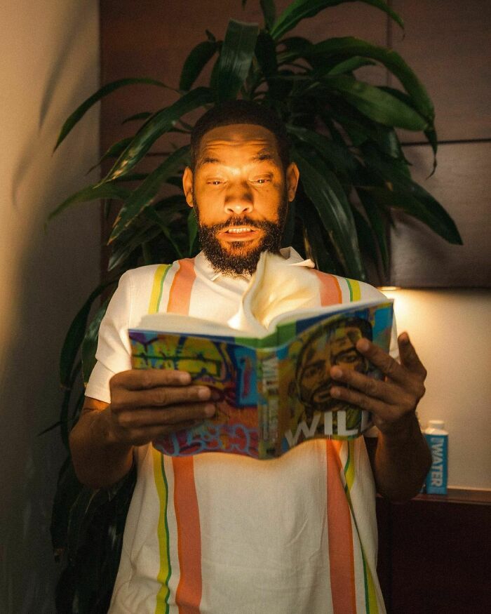 Man reading a colorful book indoors with plant in background, representing smartest celebrities and intelligence.