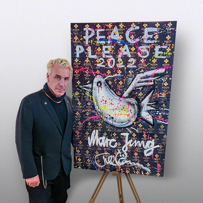 Man standing next to colorful peace-themed artwork, representing talented and intelligent celebrities in creative fields.