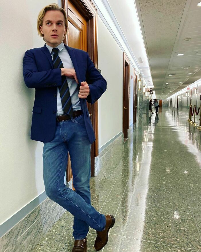 Young celebrity in a blazer and tie, standing confidently in a hallway, representing smart and intelligent celebrities.