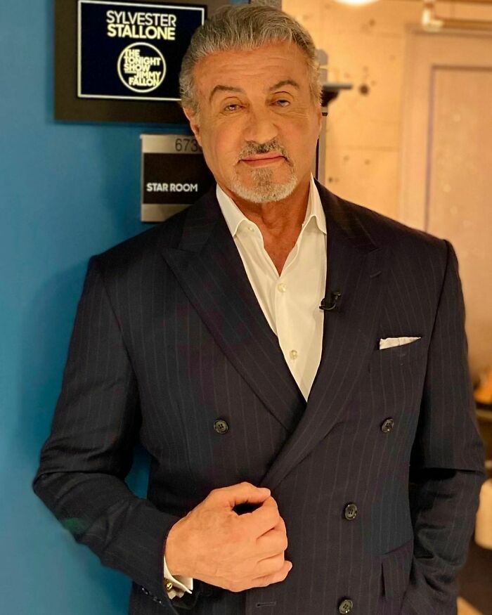 Sylvester Stallone standing in a suit backstage in a Star Room, representing smartest celebrities and intelligence.