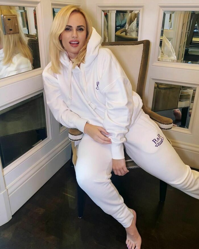 Blonde celebrity dressed in white casual clothes sitting on chair in a room with mirrors, representing smartest celebrities.