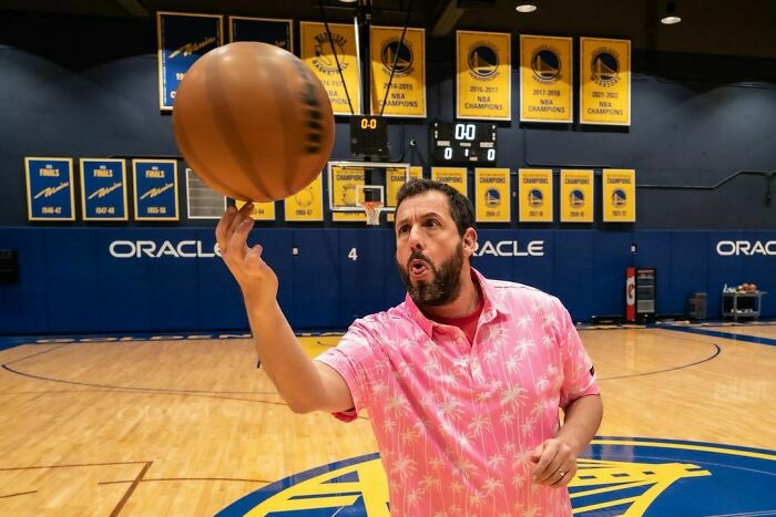 Celebrity spinning basketball on finger in indoor court, showcasing talent and intelligence in a sports setting.