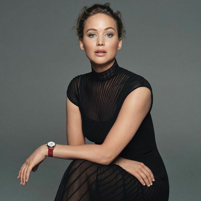 Celebrity wearing a black sheer dress and red watch, posing confidently as one of the smartest celebrities known for talent and intelligence