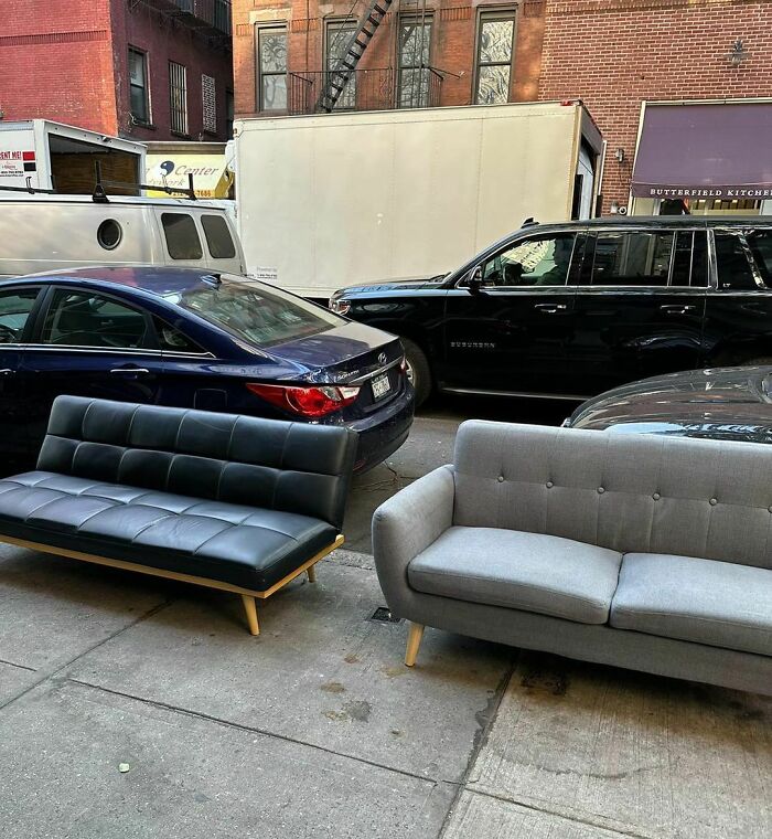 Two couches placed on a city sidewalk next to parked cars illustrating people finding treasure in thrown away items.