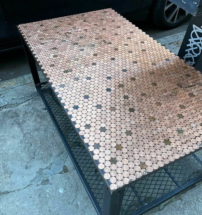 Metal table with a top surface covered in hundreds of pennies, showcasing creative repurposing of thrown away items.