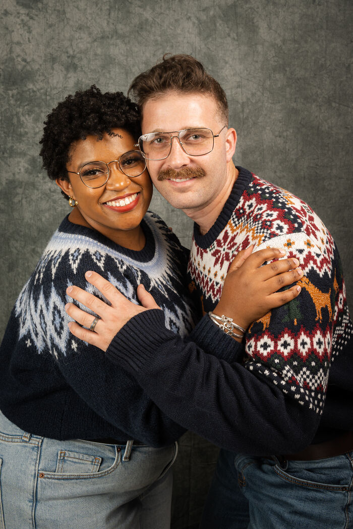 Couple posing in 80's style attire for an anniversary photoshoot, wearing matching patterned sweaters and glasses.